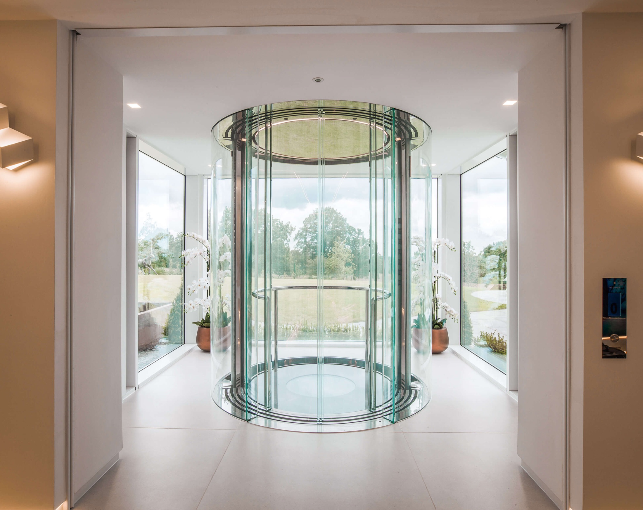 Bespoke circular scenic glass lift in a bright, garden-facing hall
